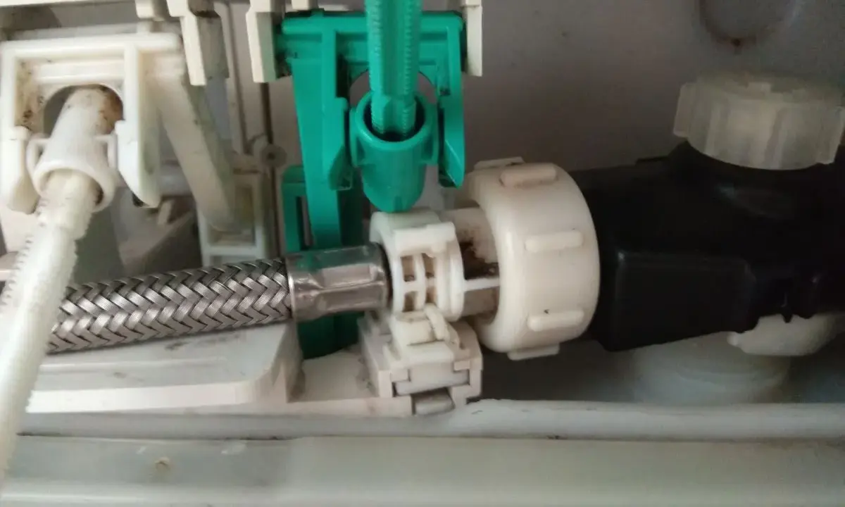 Mechanizm spłuczki Geberit, gdzie widać metalowy wężyk i zielony element. Spłuczka Geberit nie odbija, co może być spowodowane tym mechanizmem.