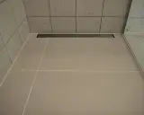 Nowoczesny prysznic z płytkami i odpływ liniowy bez koperty, który dyskretnie odprowadza wodę.