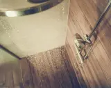 Woda leje się z prysznica na drewnianą podłogę, a w powietrzu unosi się nieprzyjemny smród z odpływu prysznica.