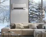 Klimatyzator grzeje, ale zimny powiew z okna przypomina o wadach ogrzewania klimatyzatorem. Wnętrze z sofą i widokiem na zimowy krajobraz.