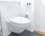 Nowoczesna, wisząca miska WC wydaje się być zamontowana za nisko, co może utrudniać korzystanie. Obok rolka papieru toaletowego.