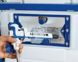 Montaż mechanizmu spłuczki podtynkowej Geberit. Dłoń trzyma biało-niebieski element zaworu.