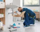Hydraulik wykonuje demontaż baterii umywalkowej, używając klucza do odkręcenia syfonu.