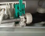 Mechanizm spłuczki Geberit, gdzie widać metalowy wężyk i zielony element. Spłuczka Geberit nie odbija, co może być spowodowane tym mechanizmem.