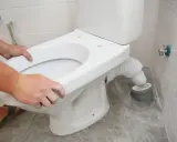 Montaż WC kompakt z odpływem pionowym: ręce dopasowują muszlę do rury odpływowej.