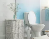 Biała, ceramiczna spłuczka WC starego typu w łazience z wiklinowym koszem i bukietem gipsówki.