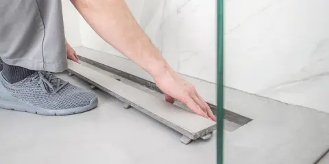 Montaż płytki w odpływie liniowym. Ręka kładzie płytkę na ramie odpływu.