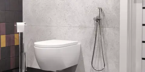 Nowoczesna łazienka z podwieszaną miską WC i bidetta na jakiej wysokości zamontowana, obok uchwyt na papier toaletowy.