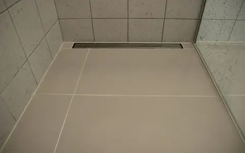 Nowoczesny prysznic z płytkami i odpływ liniowy bez koperty, który dyskretnie odprowadza wodę.