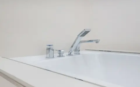 Elegancki montaż baterii wannowej na białej wannie, z chromowanymi elementami i słuchawką prysznicową.