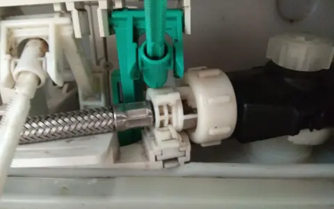 Mechanizm spłuczki Geberit, gdzie widać metalowy wężyk i zielony element. Spłuczka Geberit nie odbija, co może być spowodowane tym mechanizmem.