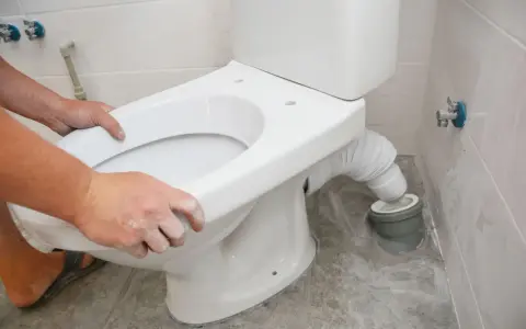 Montaż WC kompakt z odpływem pionowym: ręce dopasowują muszlę do rury odpływowej.
