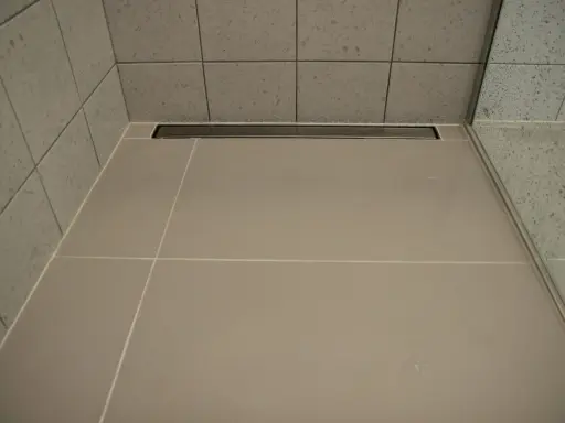 Nowoczesny prysznic z płytkami i odpływ liniowy bez koperty, który dyskretnie odprowadza wodę.