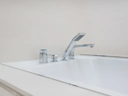 Elegancki montaż baterii wannowej na białej wannie, z chromowanymi elementami i słuchawką prysznicową.