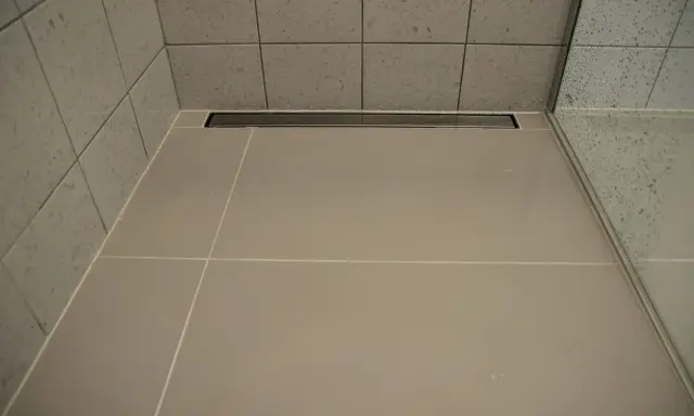 Nowoczesny prysznic z płytkami i odpływ liniowy bez koperty, który dyskretnie odprowadza wodę.