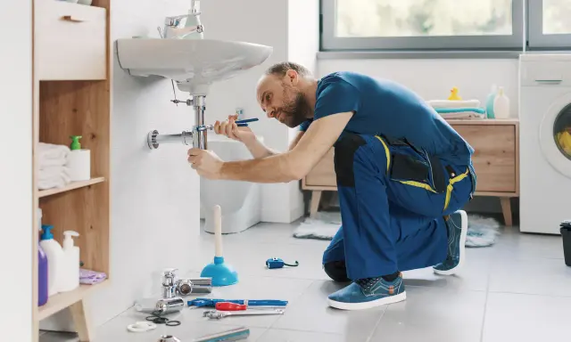 Hydraulik wykonuje demontaż baterii umywalkowej, używając klucza do odkręcenia syfonu.