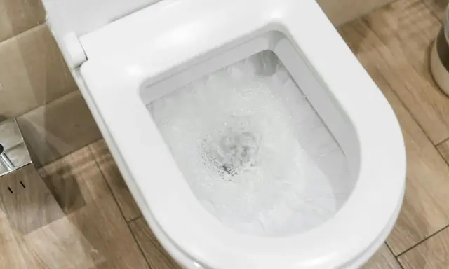 Widok na toaletę podczas spłukiwania wody. Widać wirującą wodę w muszli, co ilustruje, jak działa spłuczka.