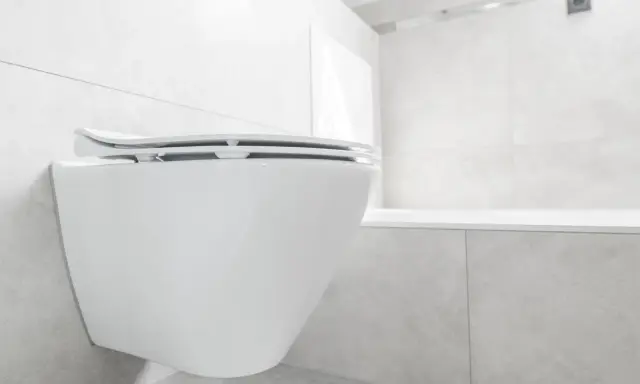 Biała, wisząca miska WC z deską wolnoopadającą. Dowiedz się, jak naprawić deskę wolnoopadającą, gdy zawiasy przestają działać.