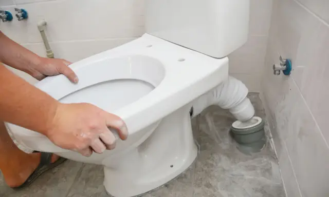 Montaż WC kompakt z odpływem pionowym: ręce dopasowują muszlę do rury odpływowej.