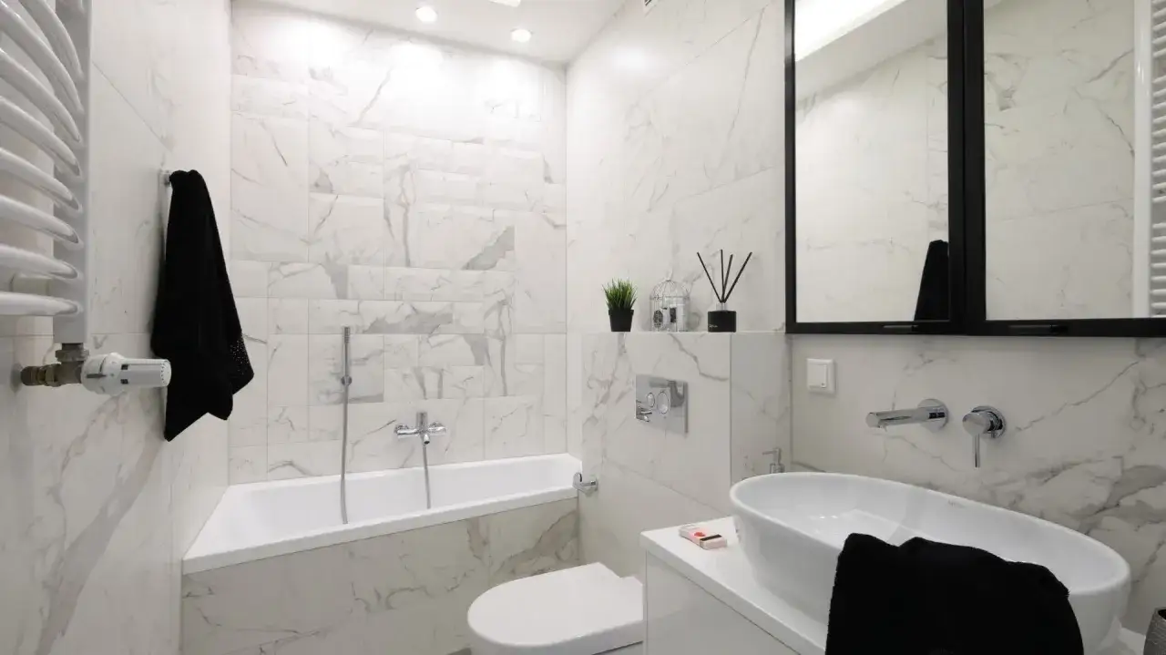Elegancka łazienka z wanną i baterią na środku. Marmurowe płytki i czarne dodatki tworzą nowoczesny styl.