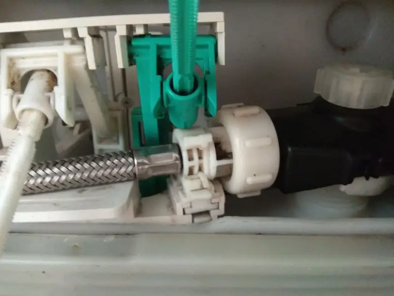 Mechanizm spłuczki Geberit, gdzie widać metalowy wężyk i zielony element. Spłuczka Geberit nie odbija, co może być spowodowane tym mechanizmem.